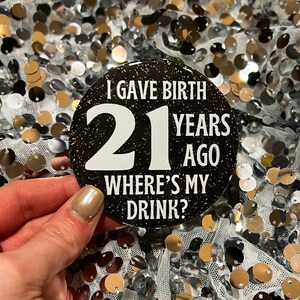 May include: Black and white round button with glitter. The button says "I gave birth 21 years ago where's my drink?"