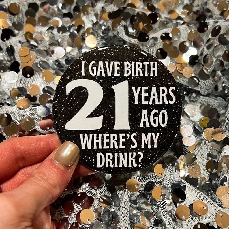 May include: Black and white round button with glitter. The button says "I gave birth 21 years ago where's my drink?"