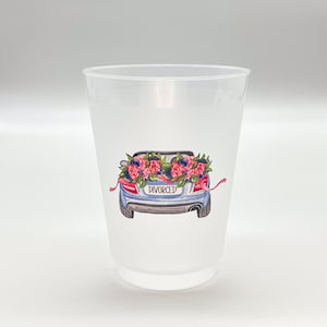 May include: A clear plastic cup with a watercolor illustration of a blue car decorated with pink and blue flowers. The car has a license plate that reads "DIVORCED". Ribbons are attached to the car.