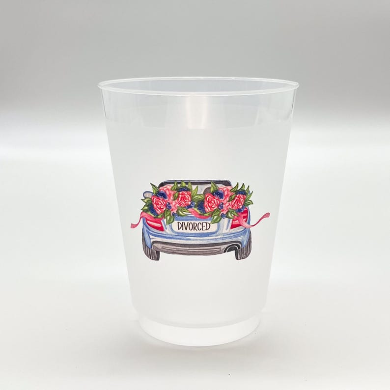 May include: A clear plastic cup with a watercolor illustration of a blue car decorated with pink and blue flowers. The car has a license plate that reads "DIVORCED". Ribbons are attached to the car.