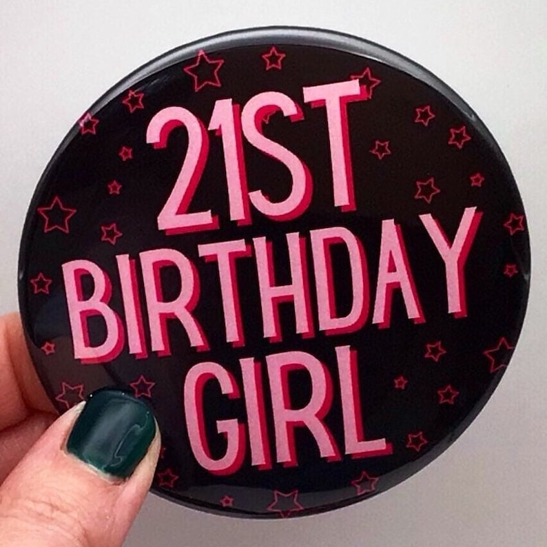 May include: A black button with pink text that reads "21st Birthday Girl" and is decorated with pink stars.