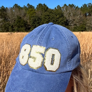 May include: A blue denim baseball cap with a white and gold glitter number "850" on the front.