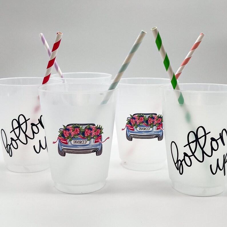 May include: Frosted plastic cups with the words "bottoms up" and a car graphic with a floral arrangement and the word "divorced". The cups have striped straws in them. A fun party favor for a divorce celebration.