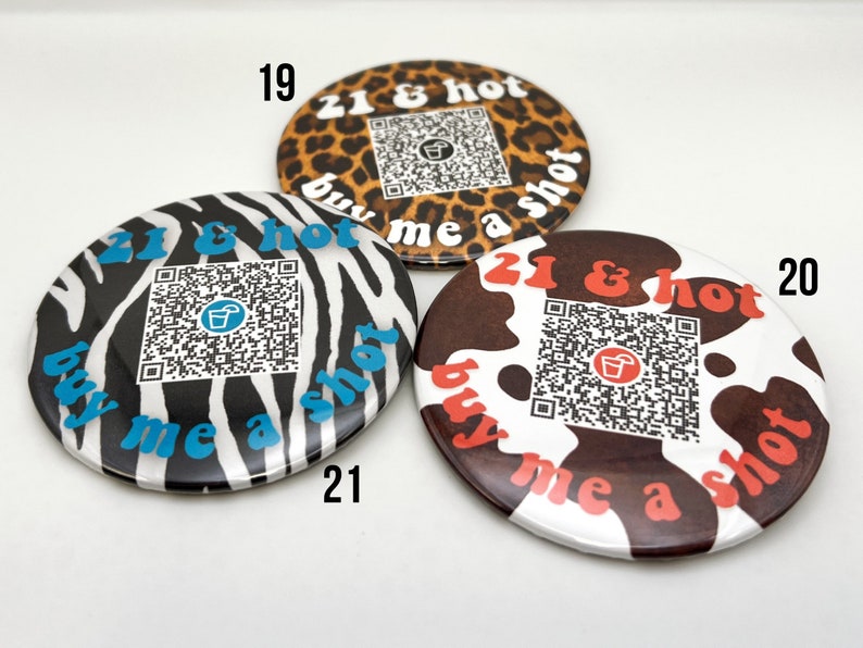 Puede incluir: Tres botones redondos con diferentes dise&ntilde;os de estampado animal. Cada bot&oacute;n tiene un c&oacute;digo QR y el texto "21 & hot buy me a shot".