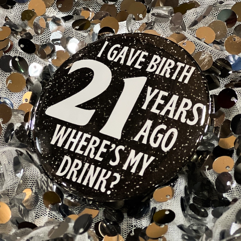 May include: Black and white button with glitter. The button says "I gave birth 21 years ago where's my drink?"