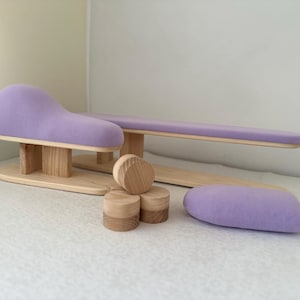 May include: A set of sewing pressing tools including a tailor's ham, a sleeve board, and three small wooden cylinders. The tools feature light-colored natural wood bases and supports with smooth, lavender-colored fabric padding on the surfaces.