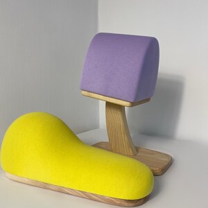 May include: Two fabric covered dress forms on wooden bases. The larger form is yellow and shaped like a crescent moon. The smaller form is purple and shaped like a half-circle.
