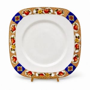 May include: Square white plate with a decorative border featuring red and yellow floral designs, set against a gold and blue background. The plate is displayed on a gold-coloured metal stand, showcasing its elegant design.