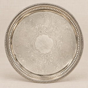 Peut inclure: Un plateau de service rond en métal argenté présentant un motif gravé complexe de fleurs et de textures quadrillées. Le plateau possède un bord en relief torsadé et une bordure ajourée décorative avec une série de petites découpes circulaires.