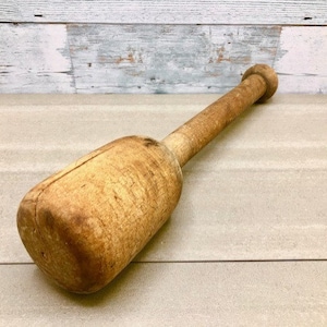 May include: A wooden mallet with a rounded head and a long handle. The mallet is worn and has a natural wood finish.