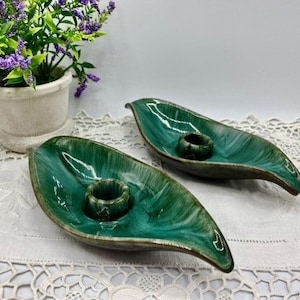 May include: Two green ceramic candle holders shaped like leaves. The holders have a glossy finish and a textured surface.