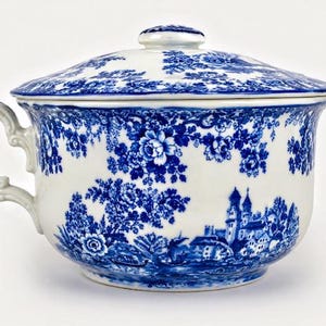 May include: A white and blue ceramic chamber pot with a lid. The pot has a blue floral and landscape design. It features a handle and a small knob on the lid.