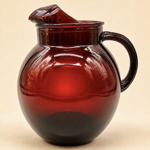Peut inclure: Une carafe en verre rouge profond de forme ronde, dotée d'un corps sphérique lisse, d'un large goulot avec un bec verseur prononcé et d'une anse incurvée robuste fixée sur le côté. Le verre translucide présente une riche teinte cramoisie.