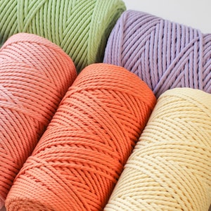 May include: Five spools of twisted cotton cord arranged in a cluster. The colors include light green, soft lavender, muted coral, vibrant orange, and pale yellow. Each spool features a tightly wound, multi-strand rope texture on a cardboard core.