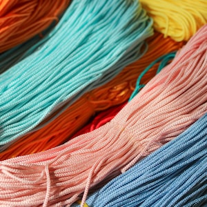 May include: Multiple bundles of thin, braided nylon cord arranged in parallel rows. The collection features a vibrant spectrum of colors including bright orange, turquoise, soft pink, sunny yellow, and deep blue, each with a smooth, textured finish.