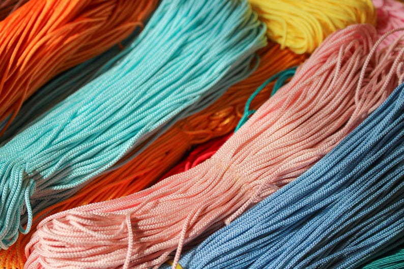 May include: Multiple bundles of thin, braided nylon cord arranged in parallel rows. The collection features a vibrant spectrum of colors including bright orange, turquoise, soft pink, sunny yellow, and deep blue, each with a smooth, textured finish.
