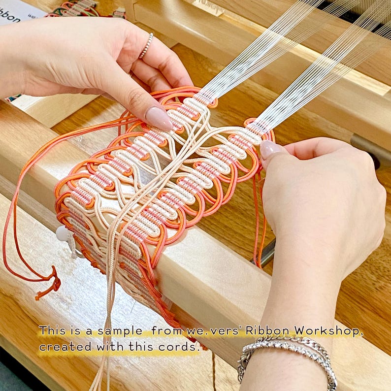 May include: A wooden weaving loom with white and orange cords being woven into a decorative pattern. The text on the image reads: This is a sample from we.vers' Ribbon Workshop, created with this cords.