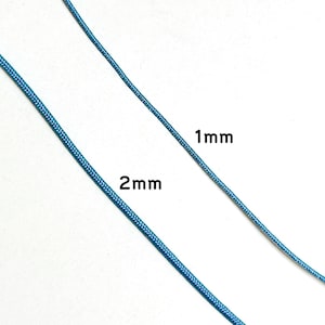 Może przedstawiać: Zbliżenie dw&oacute;ch niebieskich sznurk&oacute;w, z kt&oacute;rych jeden oznaczony jest jako "1mm", a drugi jako "2mm". Sznurki mają żywy niebieski kolor i wydają się być wykonane z tkanego materiału. Obraz podkreśla r&oacute;żnicę w grubości między dwoma sznurkami.