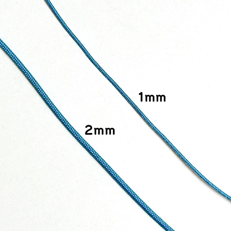 Może przedstawiać: Zbliżenie dw&oacute;ch niebieskich sznurk&oacute;w, z kt&oacute;rych jeden oznaczony jest jako "1mm", a drugi jako "2mm". Sznurki mają żywy niebieski kolor i wydają się być wykonane z tkanego materiału. Obraz podkreśla r&oacute;żnicę w grubości między dwoma sznurkami.