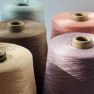 May include: Close-up of six spools of thread in various colours, including light blue, brown, pink, and purple. The spools are arranged in a semi-circle.