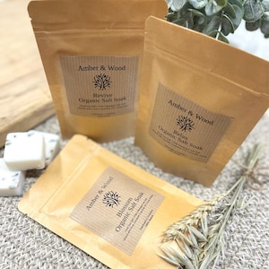 May include: Three brown paper bags with labels that read "Amber & Wood" and different scents: "Revive", "Relax", and "Blossom". Each bag contains organic salt soak.