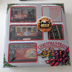 May include: A boxed Christmas train set with a red and black locomotive, carriages, and track. The box has a silver background with illustrations of snow and holly. The box reads "CHRISTMAS TRAIN" and "CAUTION-ELECTRIC TOY".