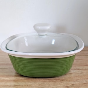 May include: A green and white ceramic casserole dish with a clear glass lid. The dish has a ribbed texture on the green exterior and a white rim. The lid has a white knob handle.