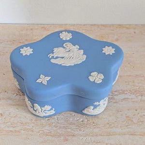 May include: A light blue, star-shaped trinket box with white relief detailing. The box features floral and classical figures in relief. The box is likely made of ceramic or porcelain.