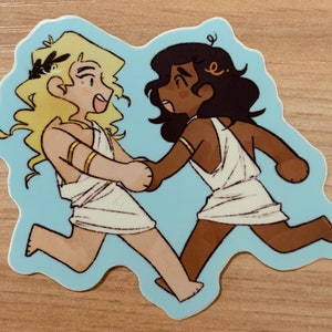 May include: A sticker featuring two cartoon figures in white togas, running and holding hands. One figure has blonde hair and a laurel wreath, the other has dark hair. The sticker has a light blue background.