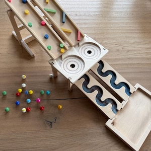 Op de afbeelding: Houten knikkerbaan met meerdere banen en kleurrijke knikkers. Het speelgoed heeft hellingen, zigzagpaden en een opvangbak. Verschillende gekleurde knikkers liggen verspreid rond de houten constructie.