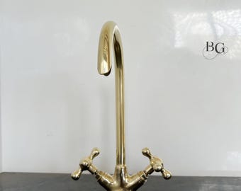 May include: A gold-toned kitchen faucet with a high spout and two cross-shaped handles.