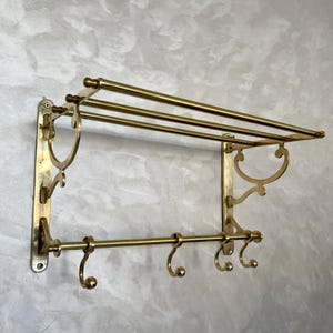 Peut inclure: Un porte-manteau mural en laiton avec une étagère et quatre crochets. Le porte-manteau a un design décoratif avec des volutes et des courbes.
