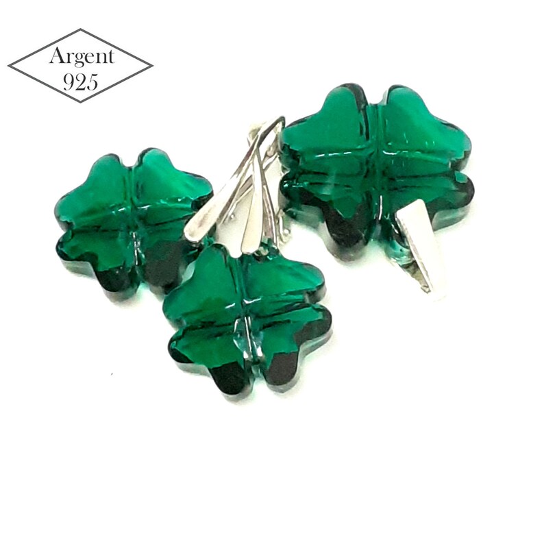 May include: Three silver clover charms with green crystal accents. The charms are attached to silver jump rings. Argent 925 is printed on a white diamond-shaped tag.