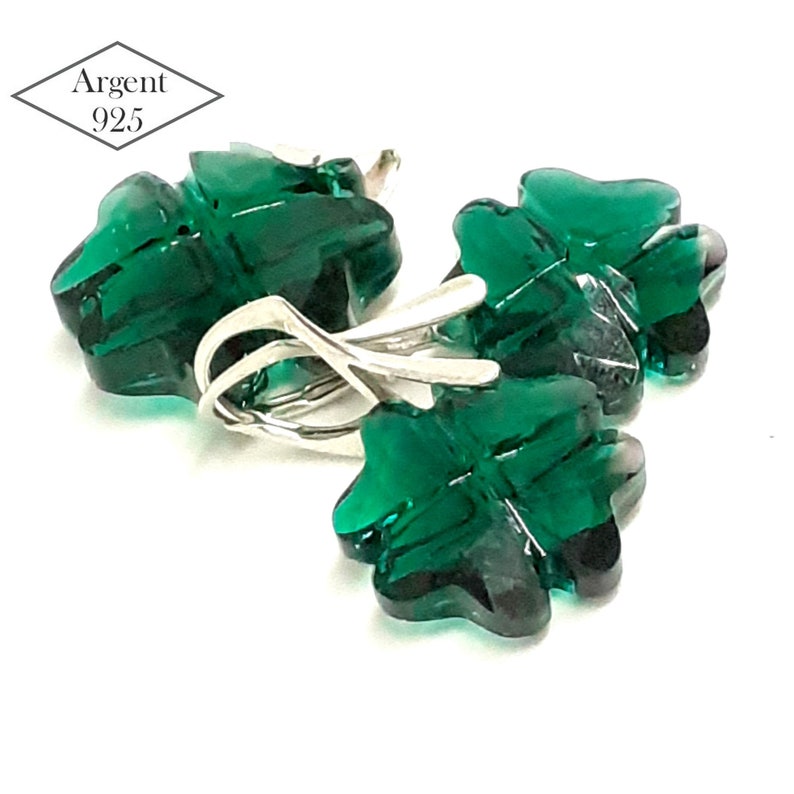 May include: A pair of silver earrings with green clover-shaped glass charms. The earrings are marked "Argent 925", indicating they are made of sterling silver.