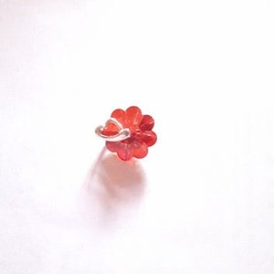 K&ouml;nnte beinhalten: Ein roter, blumenf&ouml;rmiger Nasenring mit einem silbernen Reifen.