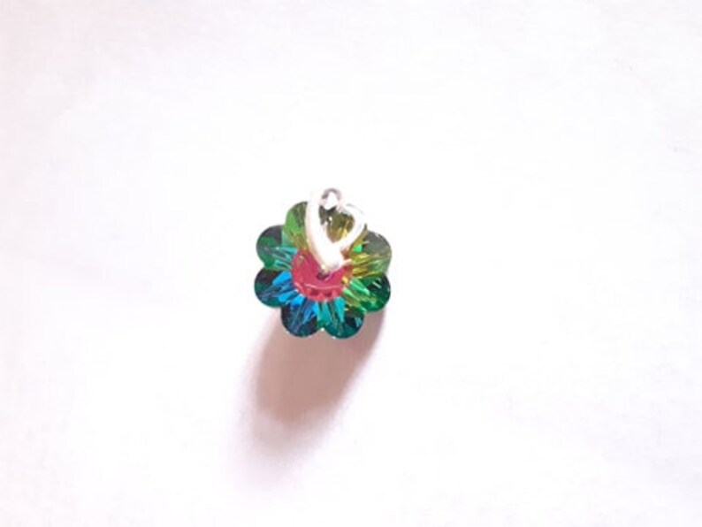 K&ouml;nnte beinhalten: Ein kleiner, mehrfarbiger Blumenanh&auml;nger mit einem silbernen Herzanh&auml;nger. Die Blume ist aus schimmerndem Glas und hat eine rote Mitte.
