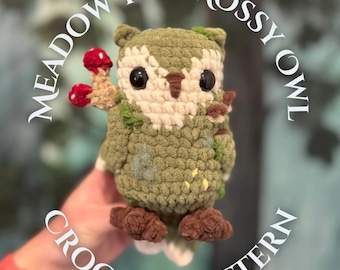 May include: A handmade crochet owl with a mossy green body, cream-colored face, and dark eyes. The owl has brown feet and is holding a small mushroom. The text "Meadow the Mossy Owl Crochet Pattern" is visible.