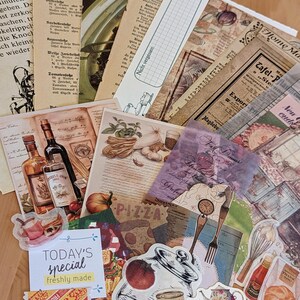 May include: A collection of vintage-style paper ephemera with a variety of designs, including a pizza slice, a jar of hash, a teapot, and a fork and knife. The papers are in shades of brown, cream, and white, with some featuring text and illustrations. The papers are arranged in a random pattern on a wooden surface.