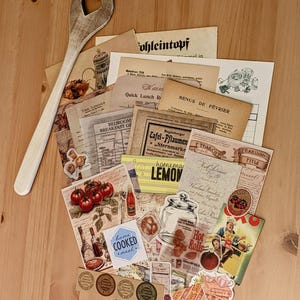 May include: A collection of vintage paper ephemera with a rustic theme. The papers feature images of food, kitchen items, and text in various languages. There are also several stickers with vintage designs. The papers are arranged on a wooden surface with a wooden spoon.
