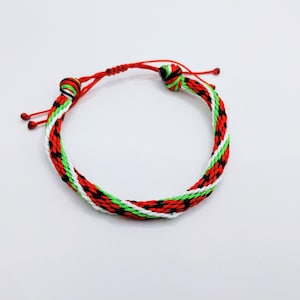 May include: Woven bracelet with red, green, black, and white threads. The bracelet has a braided design and a red adjustable closure. This handmade bracelet is a colourful accessory.