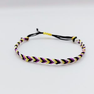 May include: A black, white, yellow and purple braided friendship bracelet.