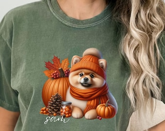 May include: A green t-shirt with a cute cartoon image of a dog wearing a fall-themed outfit. The dog is holding a small pumpkin and surrounded by fall leaves. The text "sam" is printed on the shirt.