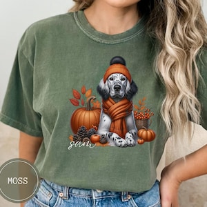 May include: A green t-shirt with a white and black dog wearing a brown and orange hat and scarf. The dog is sitting in front of a pumpkin and fall leaves. The text "Sam" is printed on the shirt.