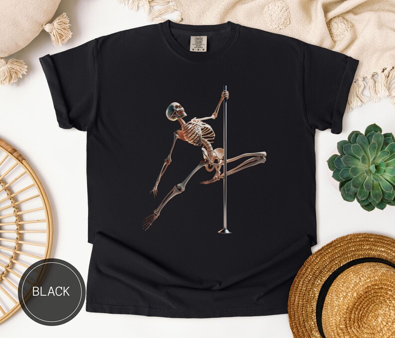 May include: Black t-shirt featuring a skeleton figure pole dancing. The skeleton is brown and white, with a blue cap. The pole is silver. The word "BLACK" is printed in a black circle at the bottom left.