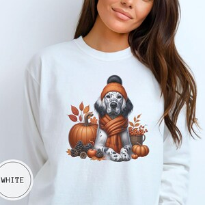 May include: White sweatshirt with a graphic of a dog wearing a brown and orange hat and scarf, surrounded by fall leaves, pumpkins, and acorns.
