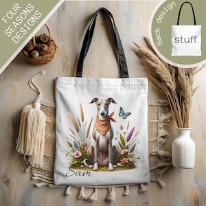 May include: White tote bag featuring a seated greyhound dog wearing an orange bandana, surrounded by flowers and tall grass. A blue butterfly is to the right of the dog. The bag has black handles and the word "Sam" is written below the dog.