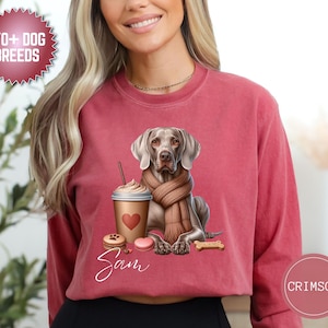 Puede incluir: Sudadera de color carmesí con un perro Weimaraner con bufanda, una taza de café, caramelos en forma de corazón y un hueso. El nombre "Sam" está escrito en cursiva. También incluye el texto "170+ DOG BREEDS".
