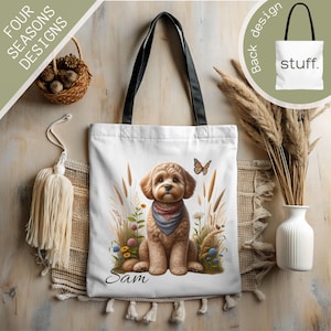 May include: White canvas tote bag featuring an illustration of a brown and white dog. The dog is wearing a blue bandana and is surrounded by flowers and grass. The text "Sam" is printed below the dog.