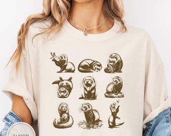 May include: Ivory-colored t-shirt featuring a sepia-toned illustration of various ferrets in different poses. The design includes ferrets eating, sleeping, and interacting. The word "IVORY" is printed on a circular label at the bottom left.