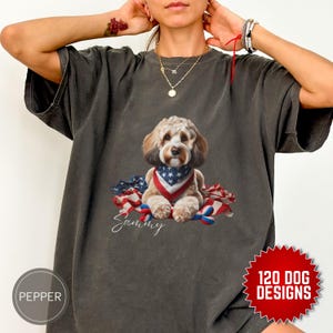 Puede incluir: Una camiseta gris con un perro lindo que lleva una bandana roja, blanca y azul y está sentado en una bandera roja, blanca y azul. El nombre del perro es Sammy.